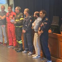 Gruppo di professionisti in divisa sul palco, in posa per la foto, con abiti da lavoro e uniforme blu, sorrisi e atmosfera formale.