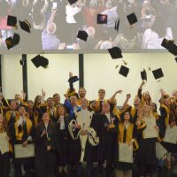 Gruppo di laureandi festanti in aula, cappelli nel cielo, felici per aver conseguito la laurea durante una cerimonia.
