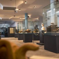 Interno di museo moderno con vetrine, illuminazione mirata e visitatori: esposizioni e percorsi museali, atmosfera tranquilla e curata.