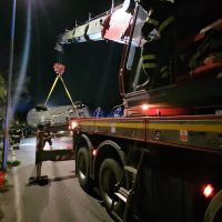 Cinque persone vengono soccorse da una gru su strada, allestimento di supporto notturno, camion e luci rosse in primo piano.