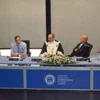 Terza conferenza: tre relatori seduti al tavolo principale con bouquet di fiori, sfondo neutro e logo sul fronte del podio.