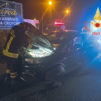Veicoli coinvolti in incidente stradale notturno, soccorritori al lavoro tra luci di emergenza e traffico. Dettagli della scena oscuri.